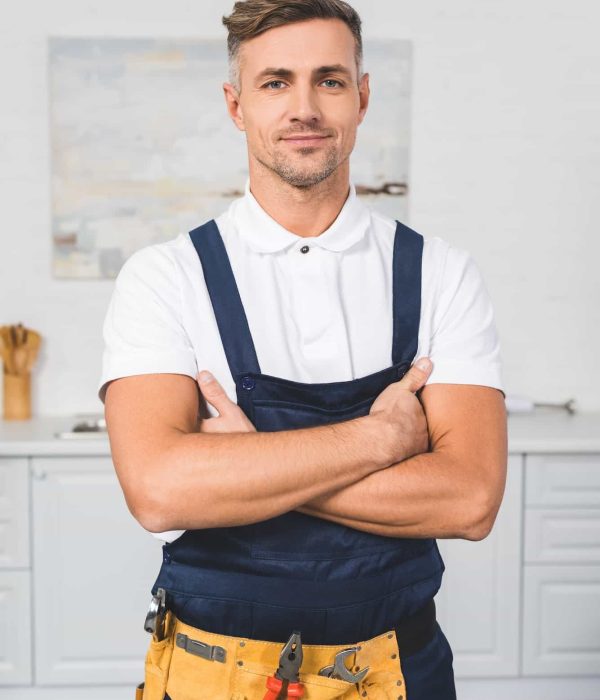 adult-repairman-in-tool-belt-standing-with-crossed-arms-at-kitchen-and-looking-at-camera.jpg